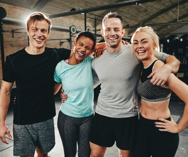 Eine fröhliche Gruppe von Fitnessstudiomitgliedern, die nach dem Training zusammen posieren und lächeln. (Wie locken Sie Leute in Ihr Fitnessstudio?)