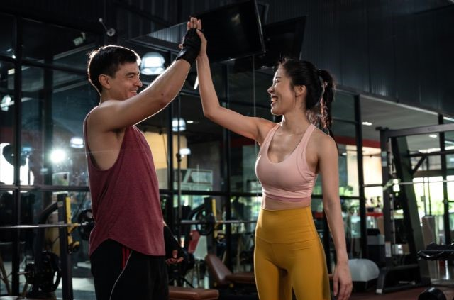 Dos personas en un gimnasio chocándose la mano, celebrando un entrenamiento exitoso. (Manteniendo a los Clientes de Entrenamiento Personal Comprometidos)