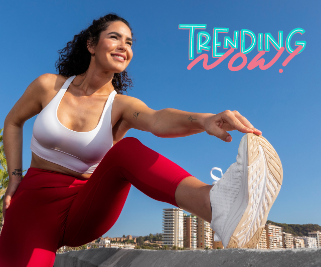 Fit woman stretching her leg outdoors against a blue sky with 'Trending Now!' text overlay, showcasing a vibrant and energetic fitness trend. (Fitness Trends)