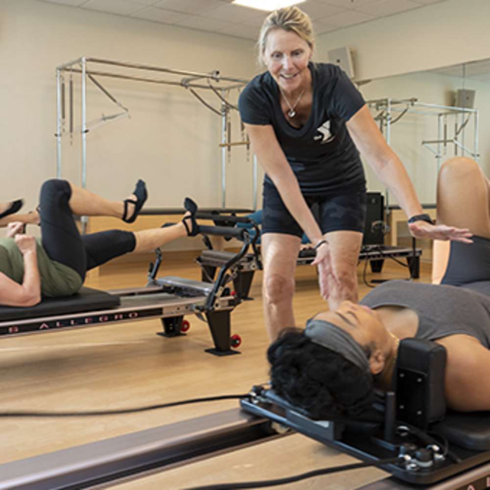 Woman pilates trainer helps the client while performing pilates exercise on the machine