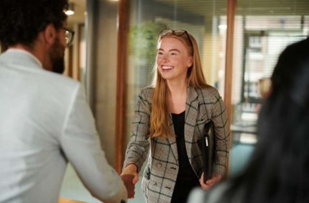 Una mujer de negocios sonriente estrechando la mano de un compañero en un entorno de oficina.
