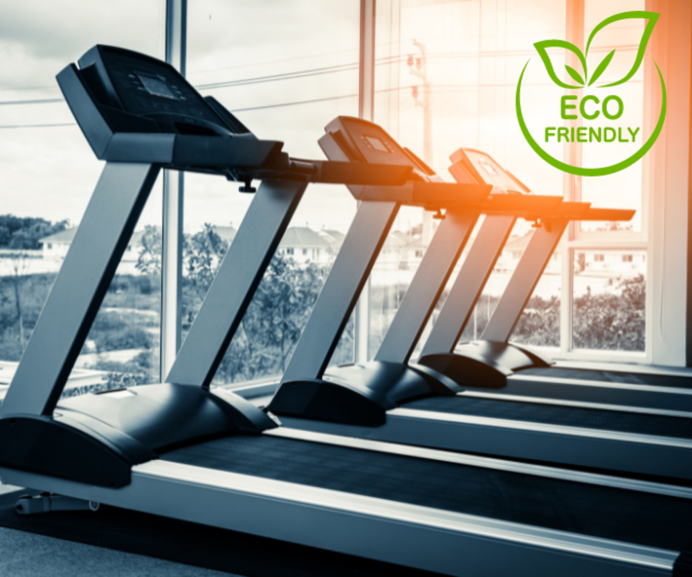 Una fila de cintas de correr ecológicas en un gimnasio con grandes ventanales que permiten la luz natural, etiquetadas con una pegatina de &quot;Eco Friendly&quot;.