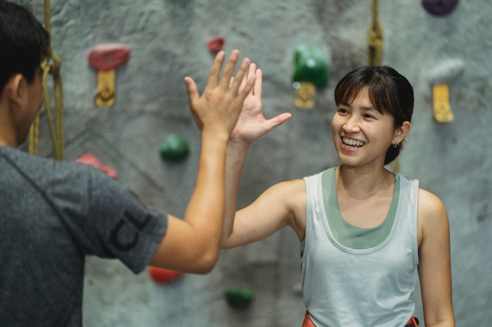 Dos escaladores en un gimnasio chocando los cinco, celebrando haber alcanzado una nueva altura o haber completado una escalada desafiante.
