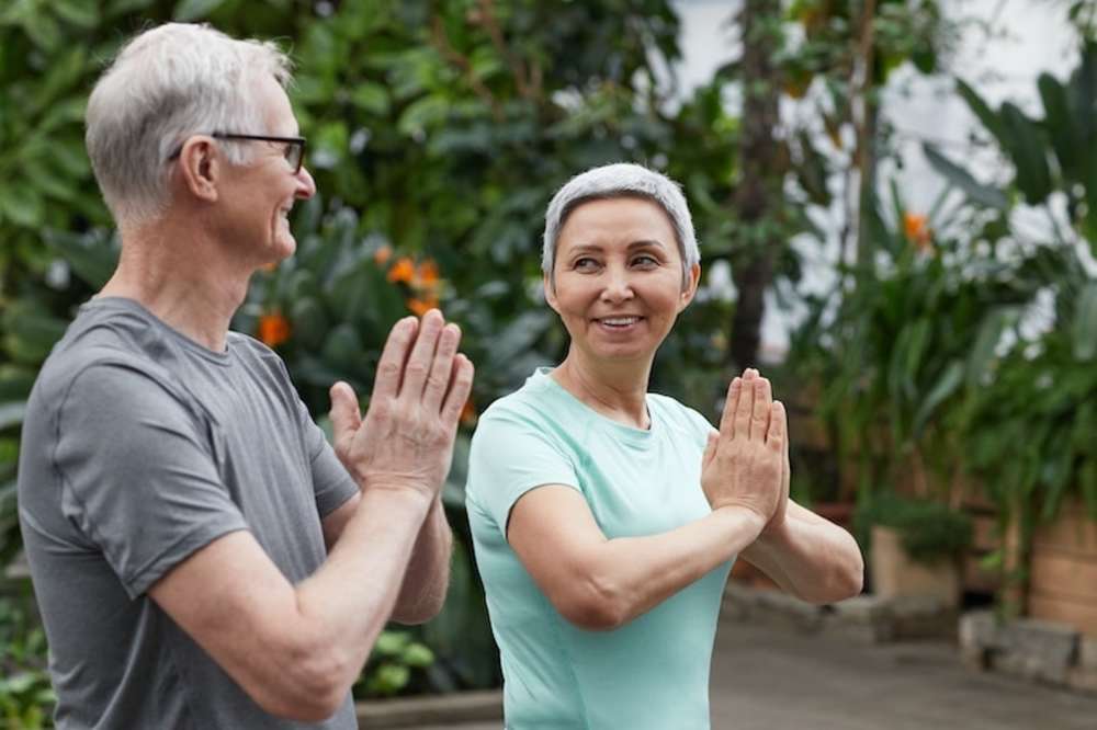 Un hombre y una mujer mayores practicando yoga juntos, sonriendo y disfrutando de su entrenamiento.