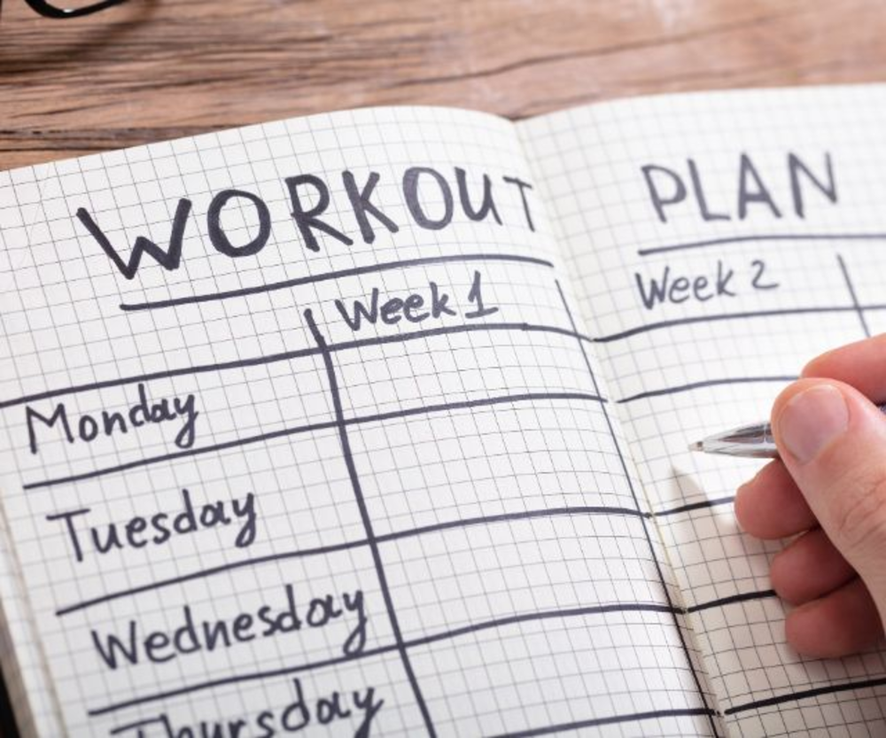 Una libreta con un plan de entrenamiento para la semana 1 y la semana 2, mostrando un horario de fitness estructurado.