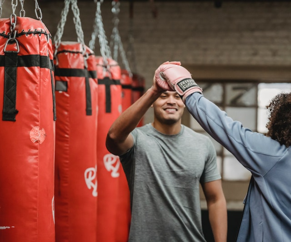 Man and woman giving high five in the boxing gloves in the boxing gym