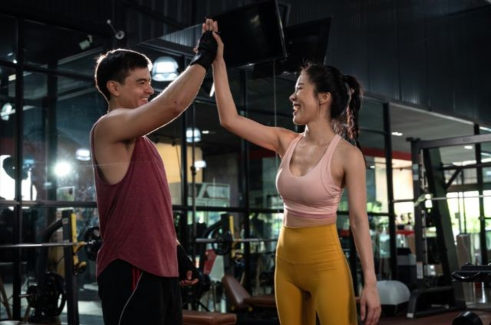 Two people in workout attire giving each other a high five in a gym setting, smiling and engaging in a friendly gesture of encouragement.