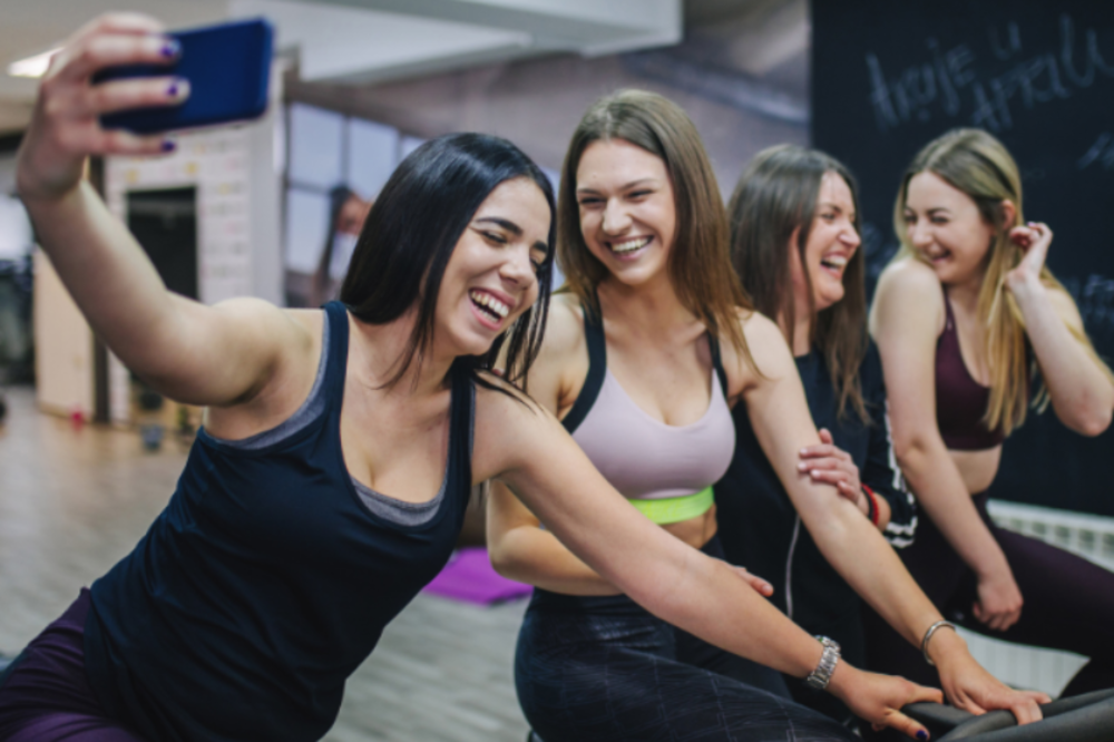 Grupo de mujeres riendo y haciéndose un selfie durante una clase en un gimnasio.