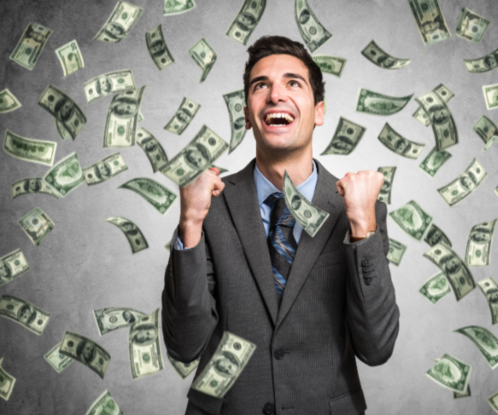 Hombre vestido de traje con los puños levantados, sonriendo, mientras cae dinero.
