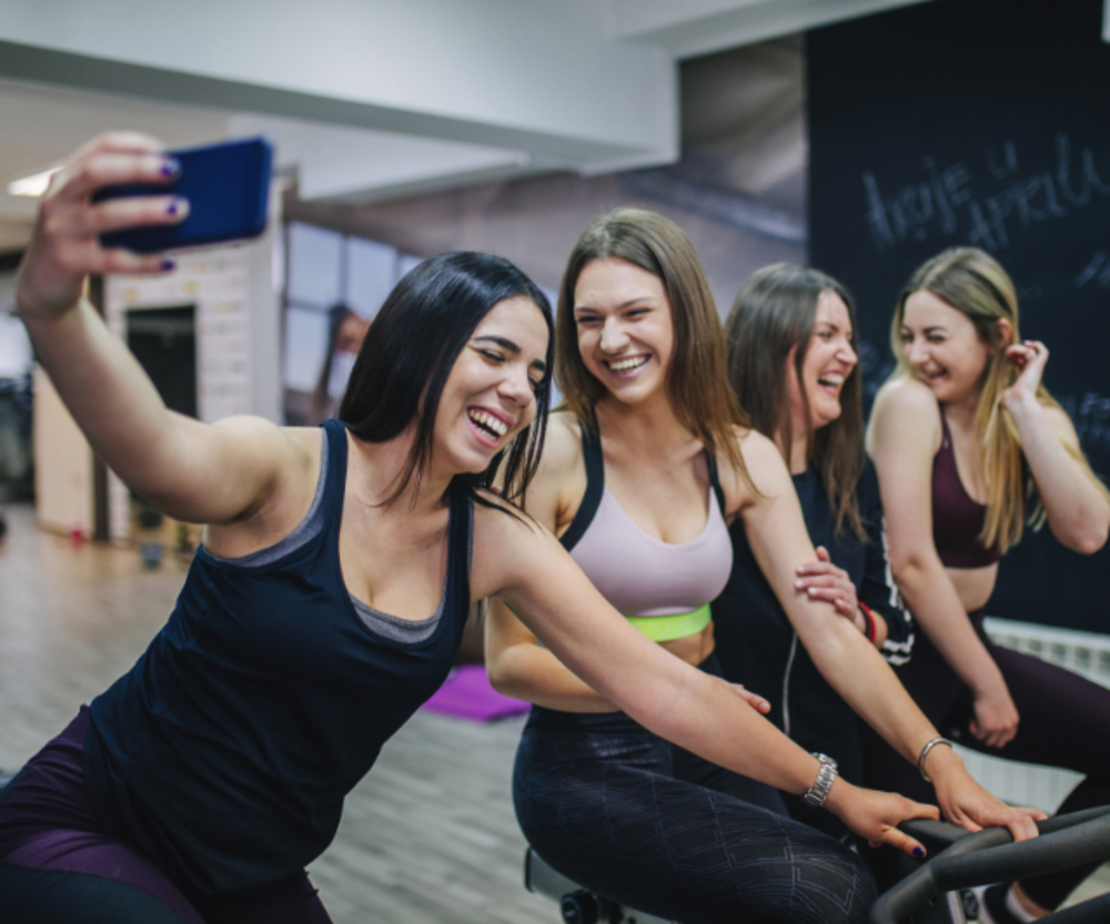 Un grupo de mujeres jóvenes tomándose un selfie en una clase de gimnasio, riendo y disfrutando de su sesión de ejercicio juntas.