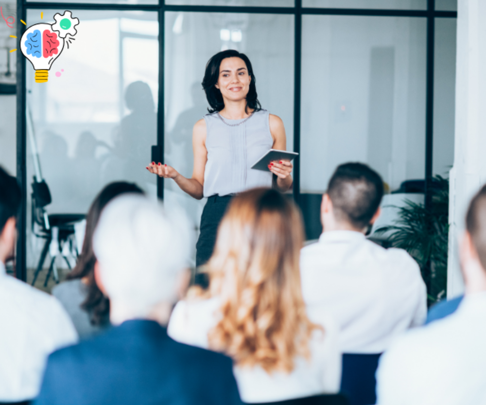 A professional woman leading a seminar, presenting with confidence to an engaged audience in a corporate setting.