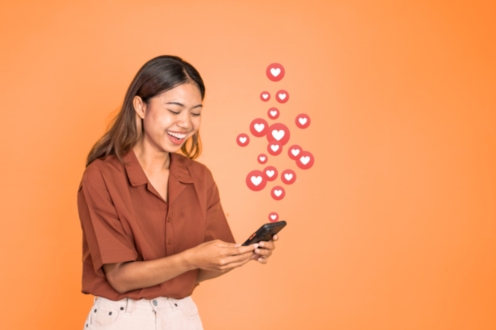 Una mujer sonriendo y mirando su teléfono, con iconos de corazón que indican likes de redes sociales flotando a su alrededor.