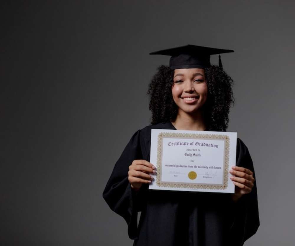 Una mujer sonriente con toga y birrete sosteniendo un certificado de graduación.