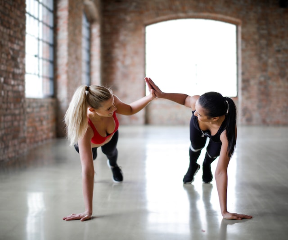 Two women are standing in plank and giving a high five to each other