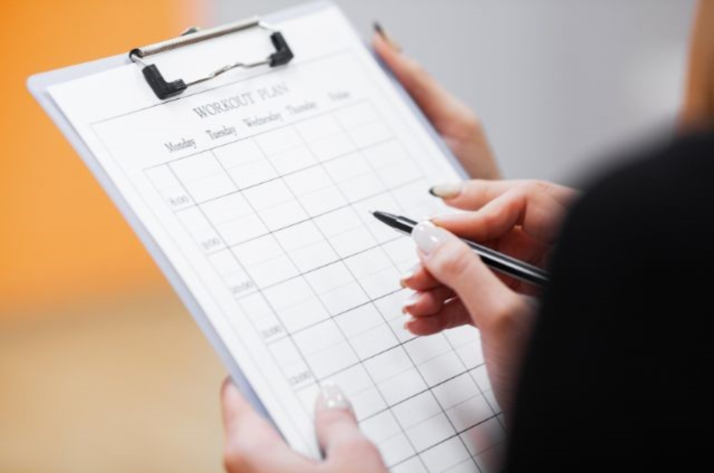 Una persona sosteniendo una tabla con un plan de entrenamiento estructurado, mostrando un horario segmentado por días y franjas horarias.
