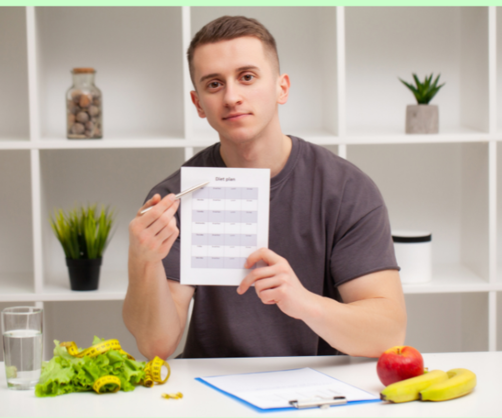 Male nutritionist showing a diet plan, with fruits, vegetables, and tape measure on desk.