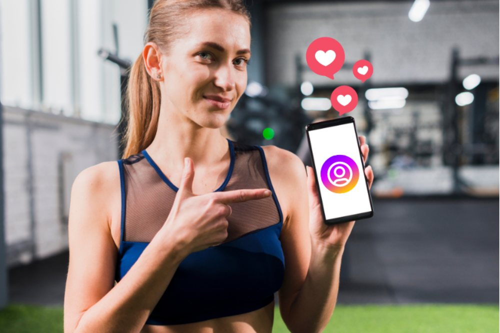 A female personal trainer in a gym pointing at her smartphone, which displays the Instagram logo