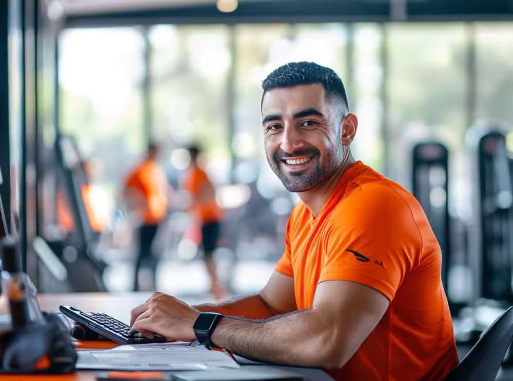 A smiling trainer managing his own business and reviewing personal trainer business plan insights in a modern gym.