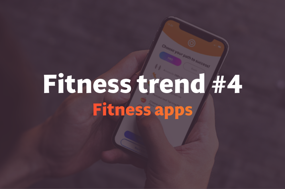 Male trainer in orange t-shirt uses his phone in a gym, illustrating how artificial intelligence supports gym members in modern fitness settings.