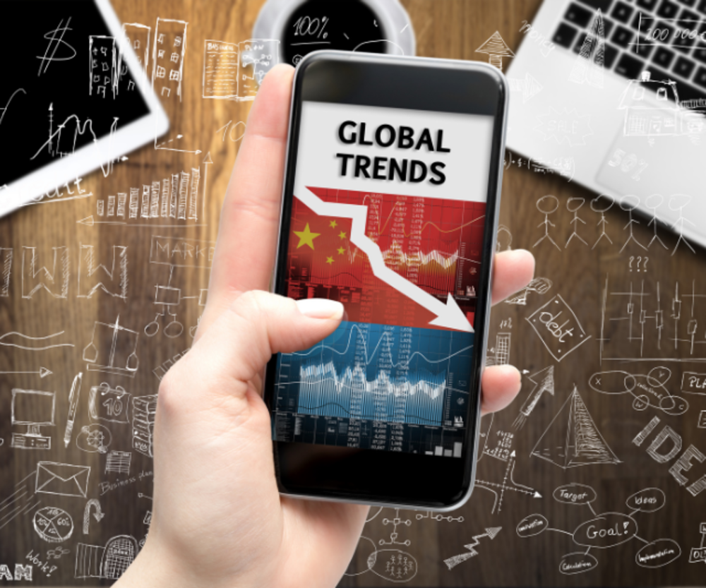 Una mano sosteniendo un móvil que muestra "Tendencias Globales" con gráficos descendentes.