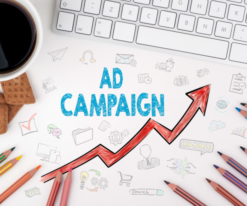 Las palabras "CAMPAÑA PUBLICITARIA" mostradas en un papel con un gráfico ascendente, reposando sobre un escritorio con un teclado y papelería.