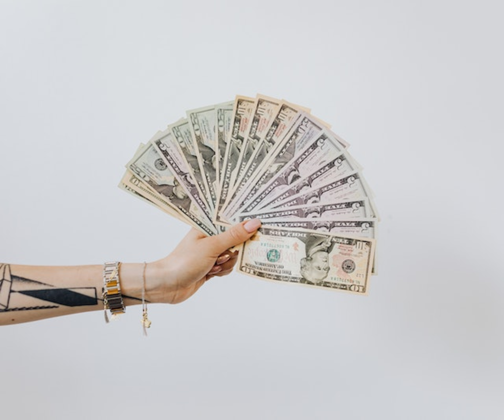 A hand displaying a fan of various U.S. dollar bills, indicating wealth or financial success.