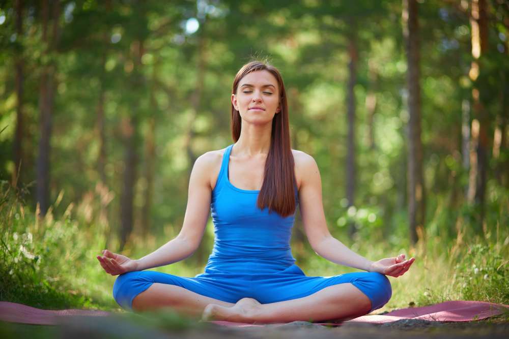 Una mujer con ropa azul meditando en un entorno tranquilo de parque.