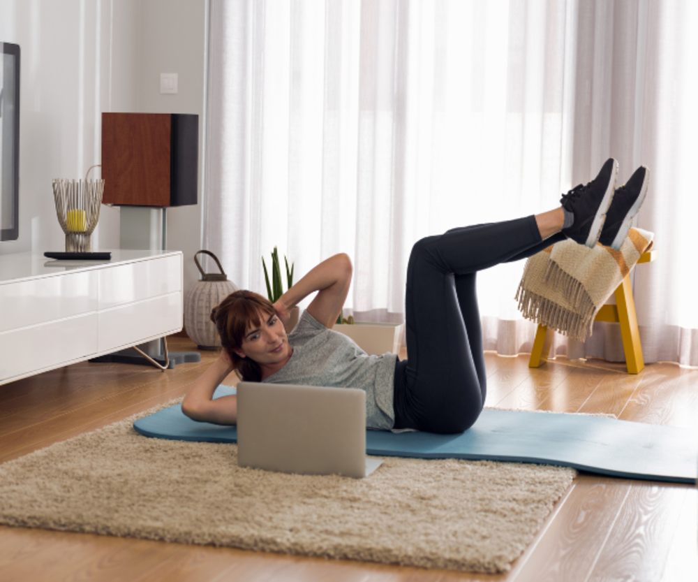 Woman doing an abdominal workout at home while watching a laptop.