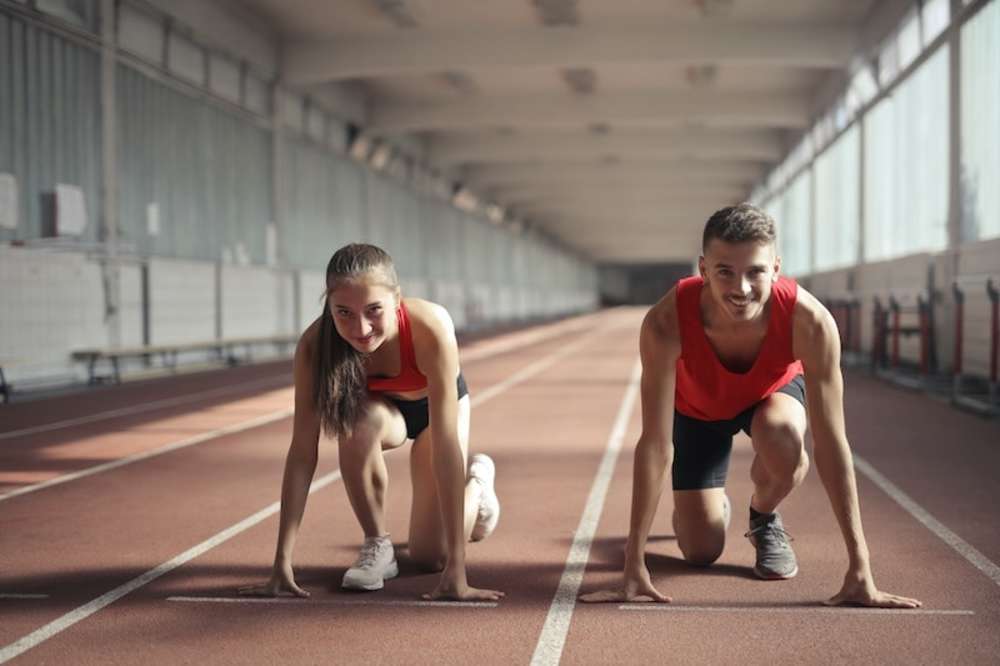 Dos jóvenes en posiciones de inicio en una pista cubierta, listos para una carrera.