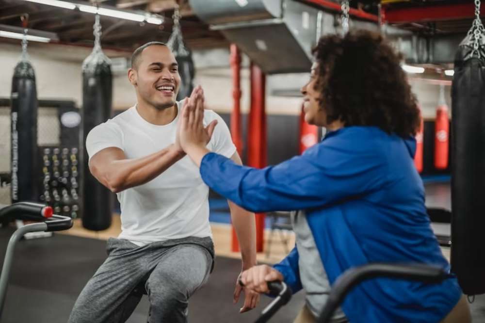 A personal trainer and a client sharing a high five in a gym setting.