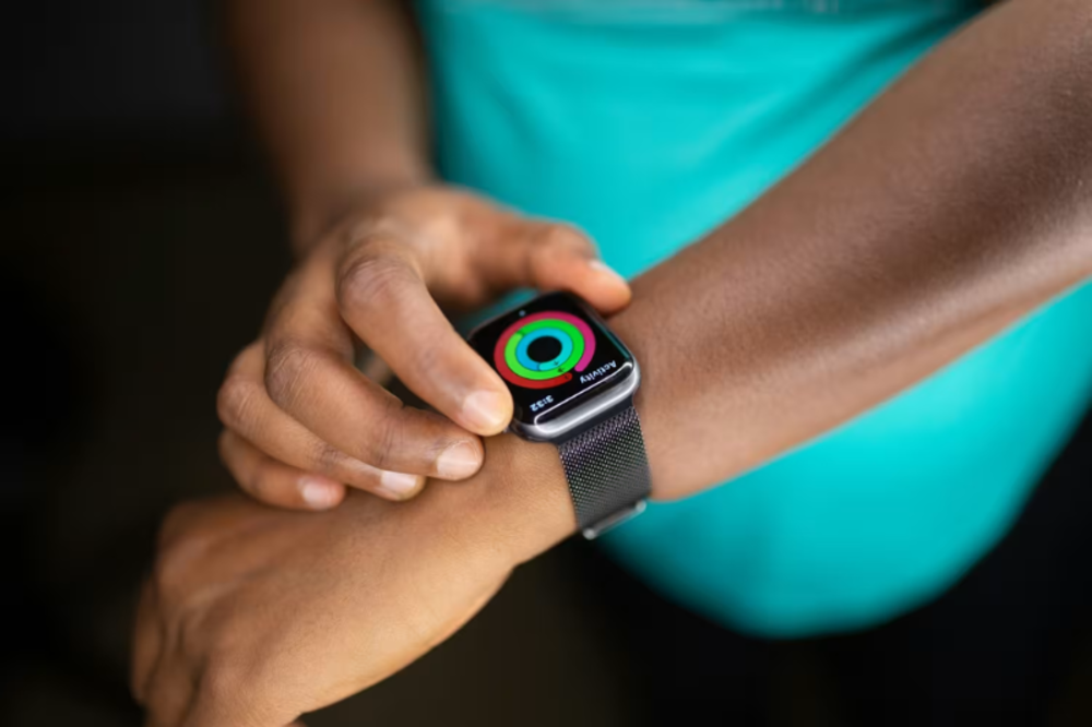 A close-up of a man’s hand as he adjusts a fitness tracker on his wrist, showing progress through activity rings.