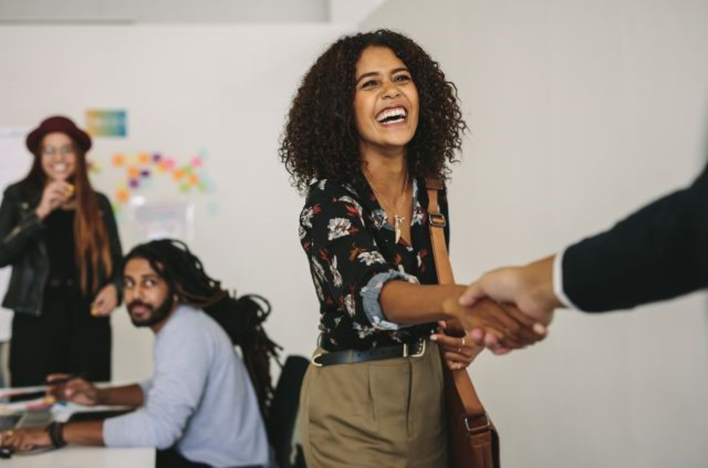 A cheerful woman shaking hands with someone, indicative of a positive meeting or agreement.