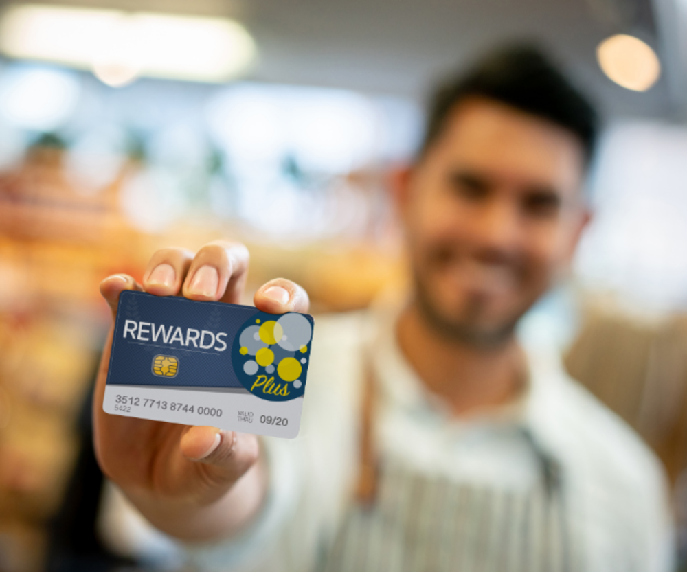 Una persona sosteniendo una tarjeta de recompensas de fidelidad en una tienda, con un fondo borroso que sugiere un ambiente de compras vibrante.