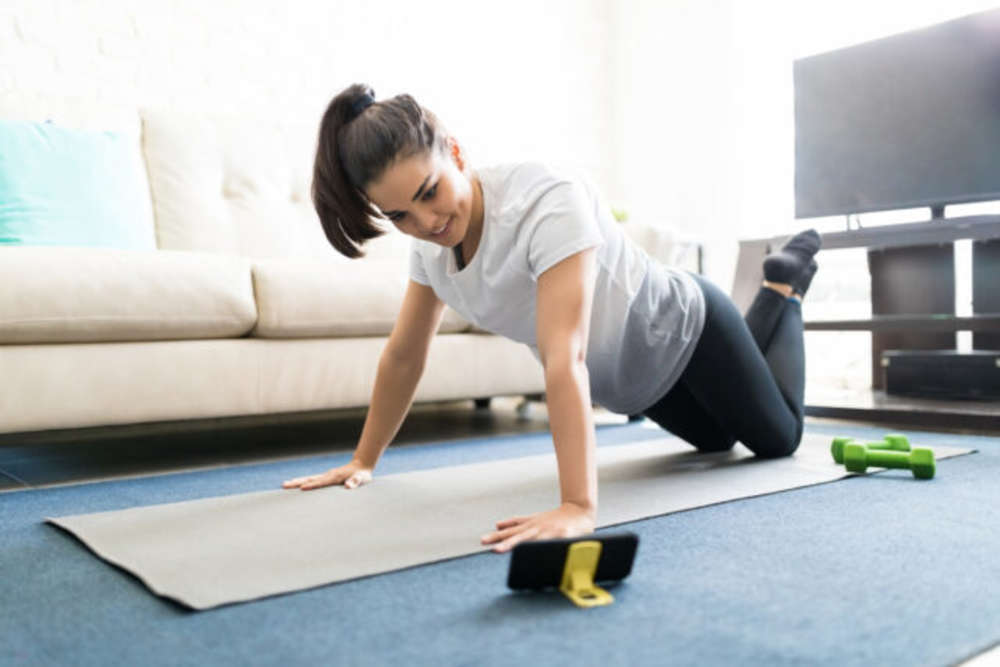 A woman exercising at home while following the workout on the smartphone.