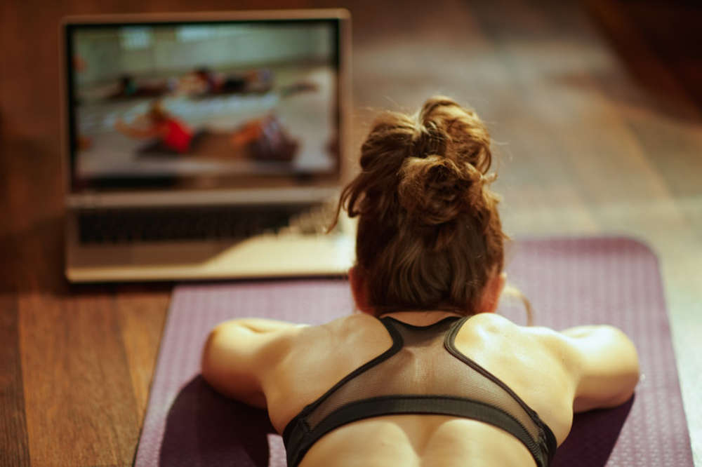 Woman having a yoga training at home by following a video workout on her laptop