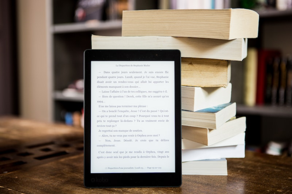 An ebook reader in front of a stack of books