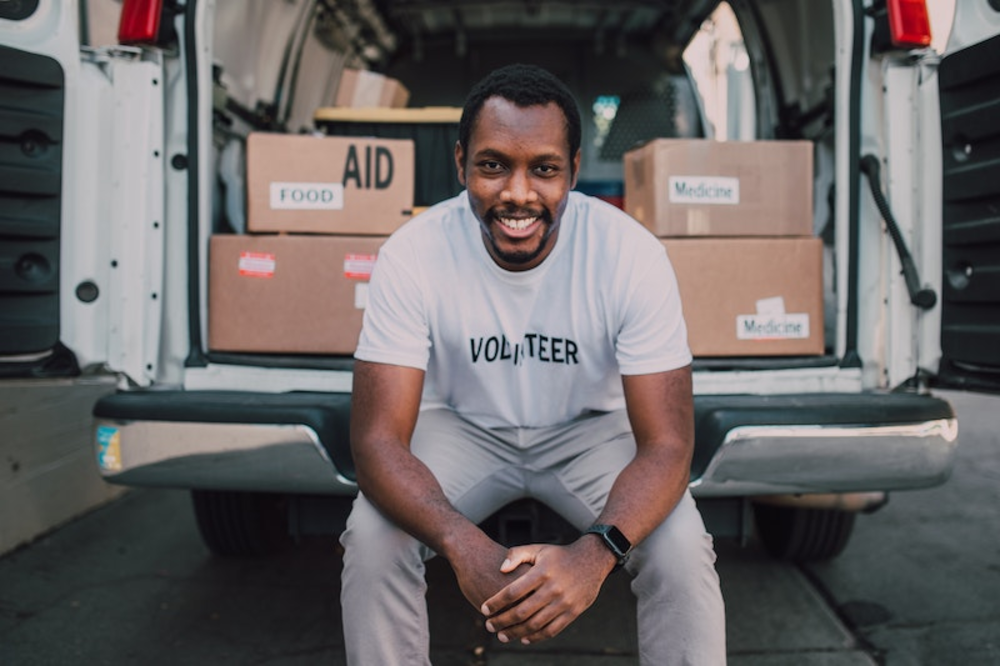 A man sitting at the back of a van with a white t-shit with a text saying volunteer