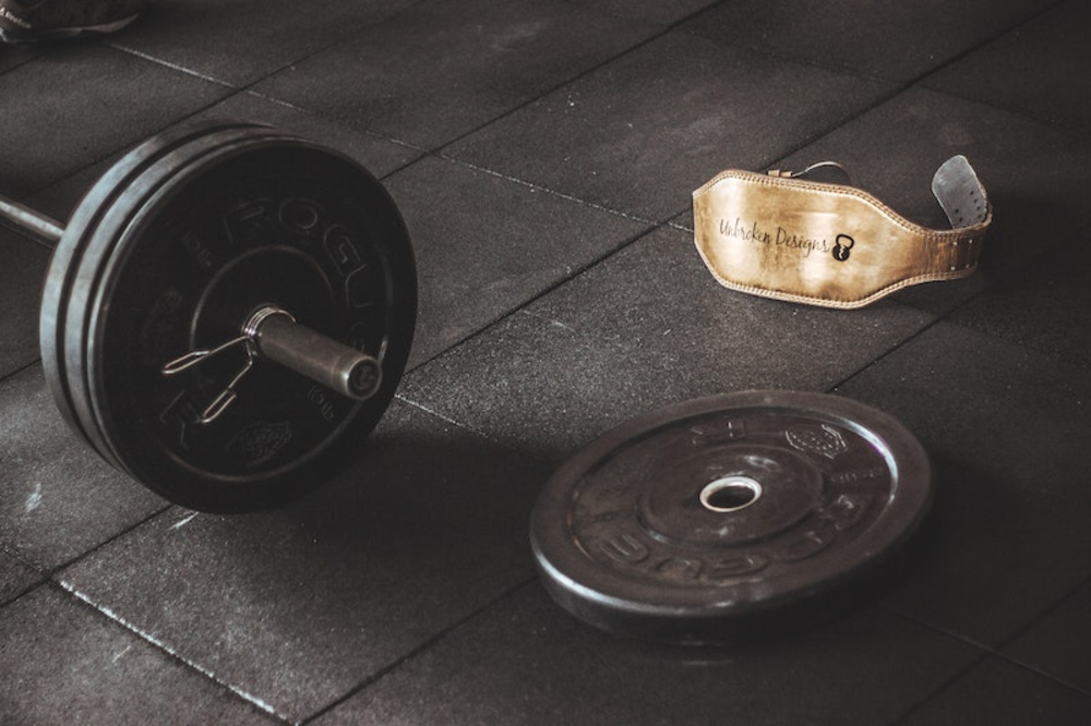 A barbell, a weight plate and a belt lying on a black floor
