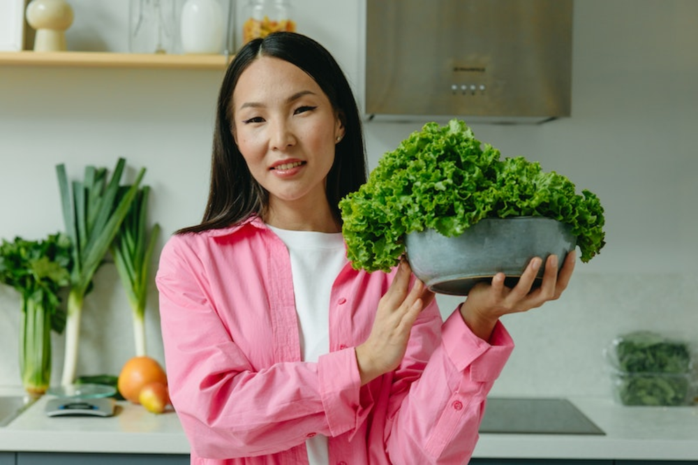 A woman holding a bowl full of green vegetables
