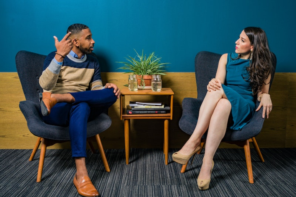 A man and a woman having a conversation while sitting on two separate chairs