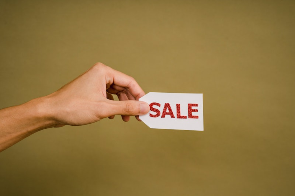 A hand holding a small sign with the text sale