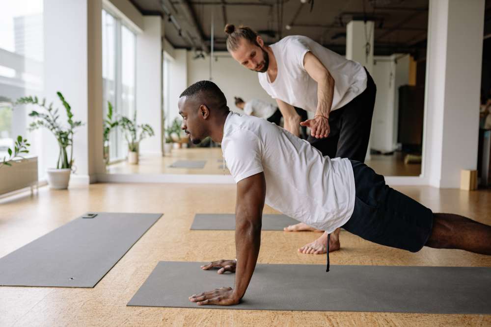 Entrenador ayuda al cliente que hace una postura de yoga