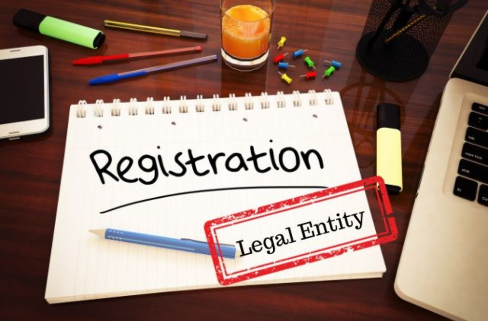 Word registration is written on the notebook paper with legal entity stamp. there also computer, pins, glass of juice, markers, pens and a phone on the table