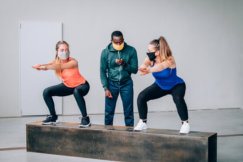 Zwei Frauen trainieren unter der Kontrolle von eine Personal Trainer, alle tragen Gesichtsmasken