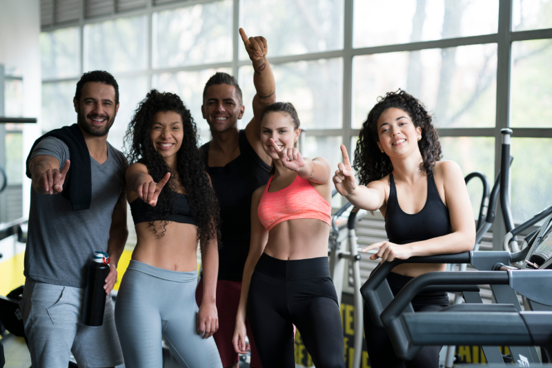 A group of happy fitness class participants posing together in a gym. (Fitness Studio Engagement Features)