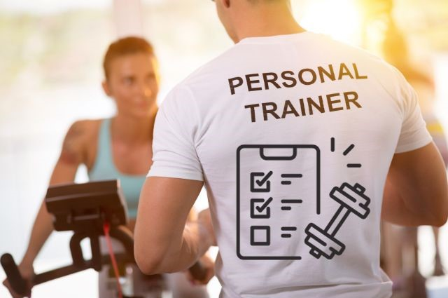 Un hombre con una camiseta de entrenador personal y una mujer en una bicicleta estática en un gimnasio