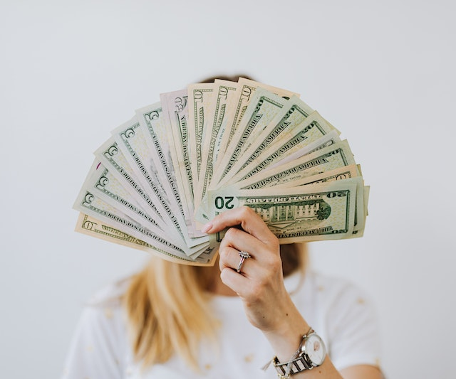 a woman holding up a bunch of money (Costs of Opening a Personal Training Business)