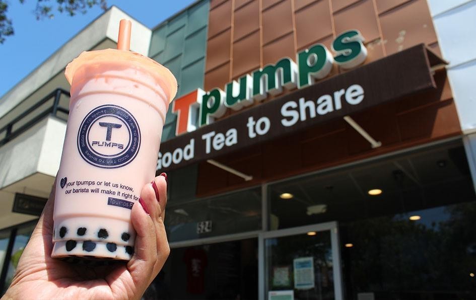 A taro drink held up in front of the store, under the “Good Tea to Share” fascia.
