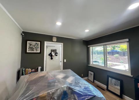 Wide living area with dark finished walls, light ceiling and trim, and furniture covered for painting.