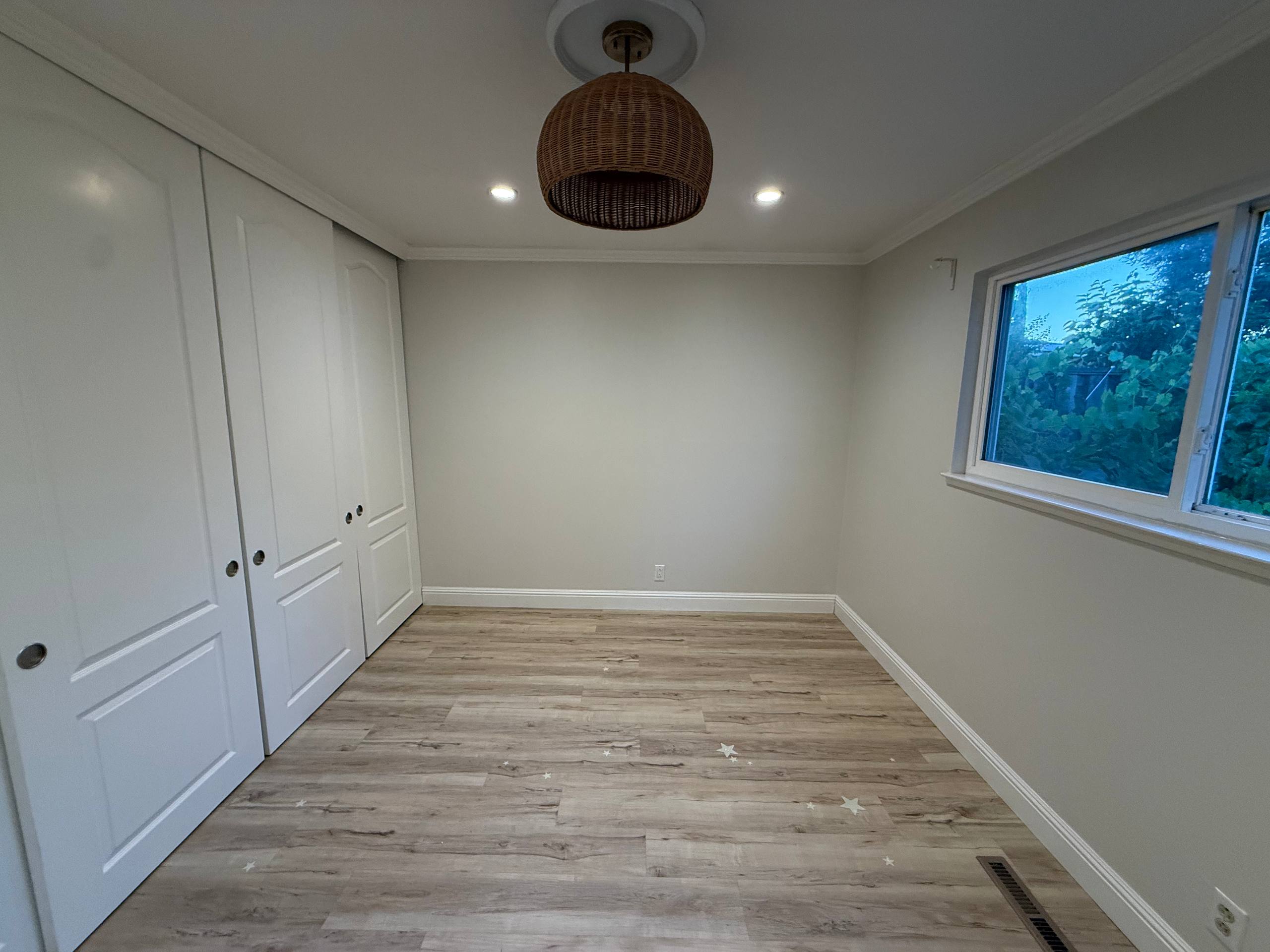 Completed empty bedroom with closed white closet doors, evenly painted walls and ceiling, trim, and window.